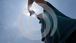 Young man drinking bottle of water standing outdoor in hot summer