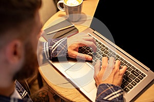 Young man drinking coffee in cafe and using laptop. Man& x27;s hands using laptop during coffee break