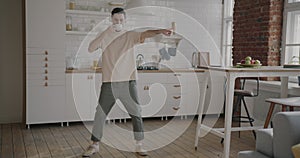 Young man drinking coffee dancing and enjoying music through headphones in kitchen at home