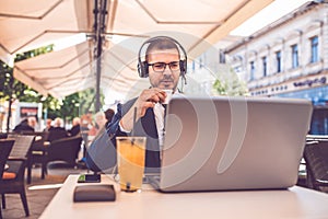 Young man drinking coffee while having a conversation on a laptop wearing a headphones