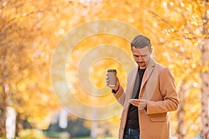 Young man drinking coffee with phone in autumn park outdoors