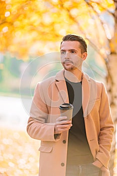 Young man drinking coffee with phone in autumn park outdoors