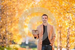 Young man drinking coffee with phone in autumn park outdoors