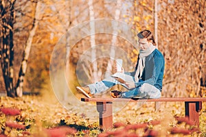 Young man drinking coffee with phone in autumn park outdoors