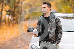 Young man drinking coffee with phone in autumn park outdoors