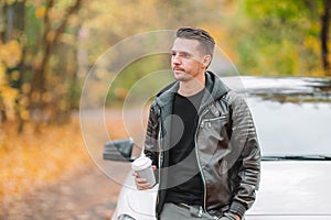 Young man drinking coffee with phone in autumn park outdoors