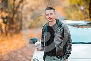 Young man drinking coffee with phone in autumn park outdoors