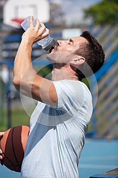 young man drinking mineral water on basketball court