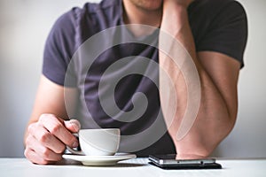 Young man drinking morning coffee and holding mobile phone. Coffee break. Man holding cup of fresh roasted coffee and looking at t