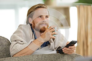 young man drinking tea and watching tv on sofa