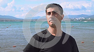 Young man drinks beer on background of people swimming in sea. Media. Attractive man relaxing on sea drinking beer. Man