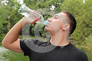 Young man drinks water on the background of beautiful green nature. quenches thirst. healthy lifestyle and health care