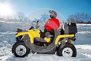 Young man driver in red warm winter clothes and black helmet on the ATV 4wd quad bike stand in heavy snow with deep