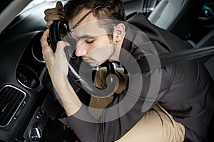 Young man is driving asleep. He is sitting at his car, his hands and head are on the steering wheel. Road safety concept