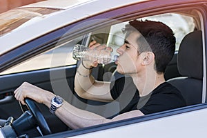 Young man driving car and drinking water from