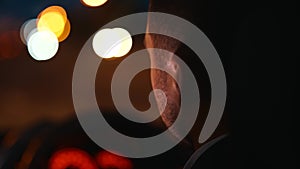 Young man driving car at night. Cropped, close up. Right hand drive car. City lights on blurred background. Traveling