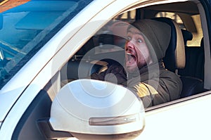Young man driving a car shocked about to have traffic accident, view from a side window