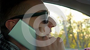 Young man driving car and speaking on mobile phone at Sunset sky at outdoor. Closeup man, guy, driver with glasses using