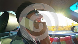 Young man driving car and speaking on mobile phone at Sunset sky at outdoor. Closeup of smiling and laughing driver