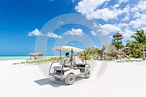 Young man driving on a golf cart at tropical white sandy beach