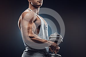 Young man with dumbbell prepare to flexing muscles over dark background