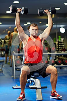 Young man with dumbbells flexing muscles in gym