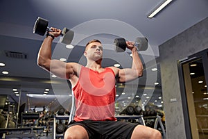 Young man with dumbbells flexing muscles in gym