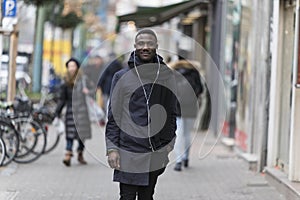 Young Man with Earphones Posing on Sidewalk with Incidental People