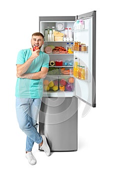 Young man eating apple near open refrigerator