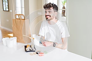 Young man eating asian sushi from home delivery looking away to side with smile on face, natural expression