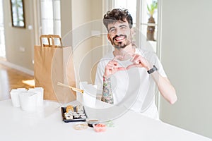 Young man eating asian sushi from home delivery smiling in love showing heart symbol and shape with hands