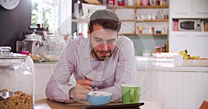 Young Man Eating Breakfast Whilst Using Digital Tablet