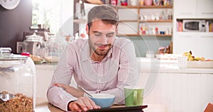 Young Man Eating Breakfast Whilst Using Digital Tablet