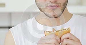 Young man is eating burger at home, mouth and hands with food closeup.