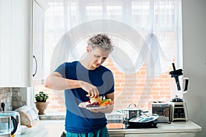 Young man eating carrot stick with hummus dip on the kitchen. Hummus served with raw vegetables on the plate. Healthy food lunch.