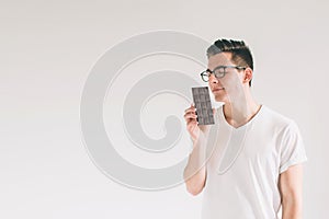 Young man eating a chocolate bar. Nerd is wearing glasses.