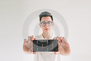 Young man eating a chocolate bar. Nerd is wearing glasses.