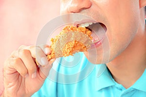 Young man eating deep fried chicken leg or drumstick