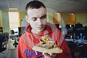 The young man eating delicious pizza against a background of office space. Fast food a break at work