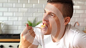 Young man eating dish from white plate. Adult guy chewing food at table in kitchen.
