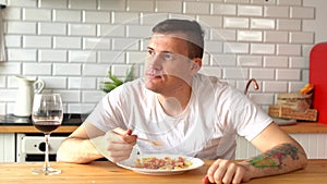 Young man eating dish from white plate. Adult guy chewing food at table in kitchen.