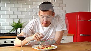 Young man eating dish from white plate. Adult guy chewing food at table in kitchen.