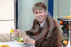 Young man eating pasta in outdoor restaurant.