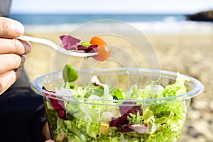Young man eating a prepared salad outdoors