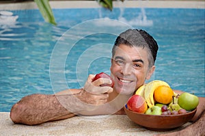 Young man eating tropical fruits behind a swimming pool