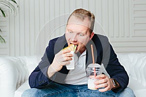A young man eats a burger and drinks a milkshake