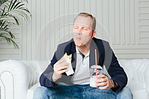 A young man eats a burger and drinks a milkshake