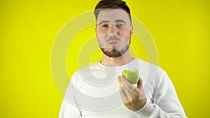 A young man eats a green apple. A man in a white sweatshirt smiles and looks at the camera. The concept of proper