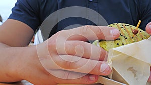 A young man eats a hamburger or cheeseburger with a green bun in an open-air cafe at a festival or village fair.