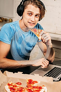 Young man eats pizza using laptop surfing internet